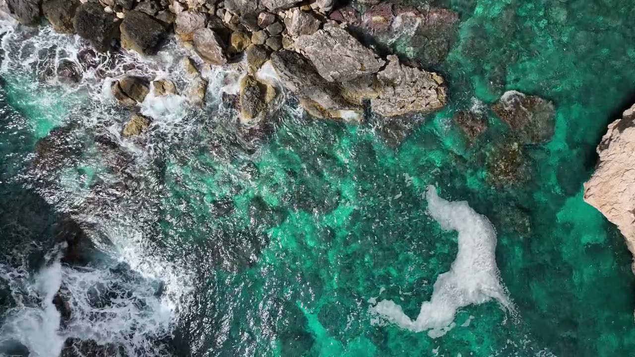 Turquoise water breaking over a rocky cove, aerial view